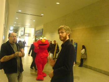 Seconds later, Giant Elmo happy-slapped Tom to the ground and kicked him in the nuts. Grant from Games Gazette on the left stood by and cheered Elmo on.